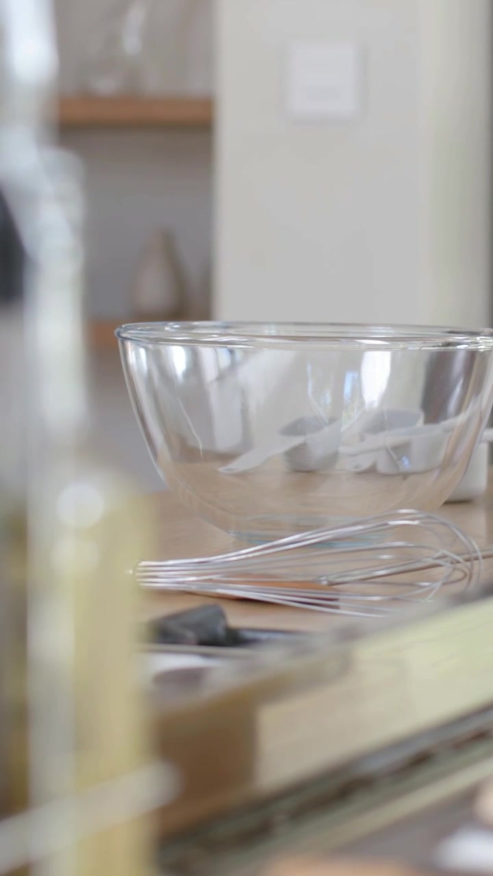 Vertical video: Shifting camera revealing glass mixing bowl whisk resting on counter showing stove