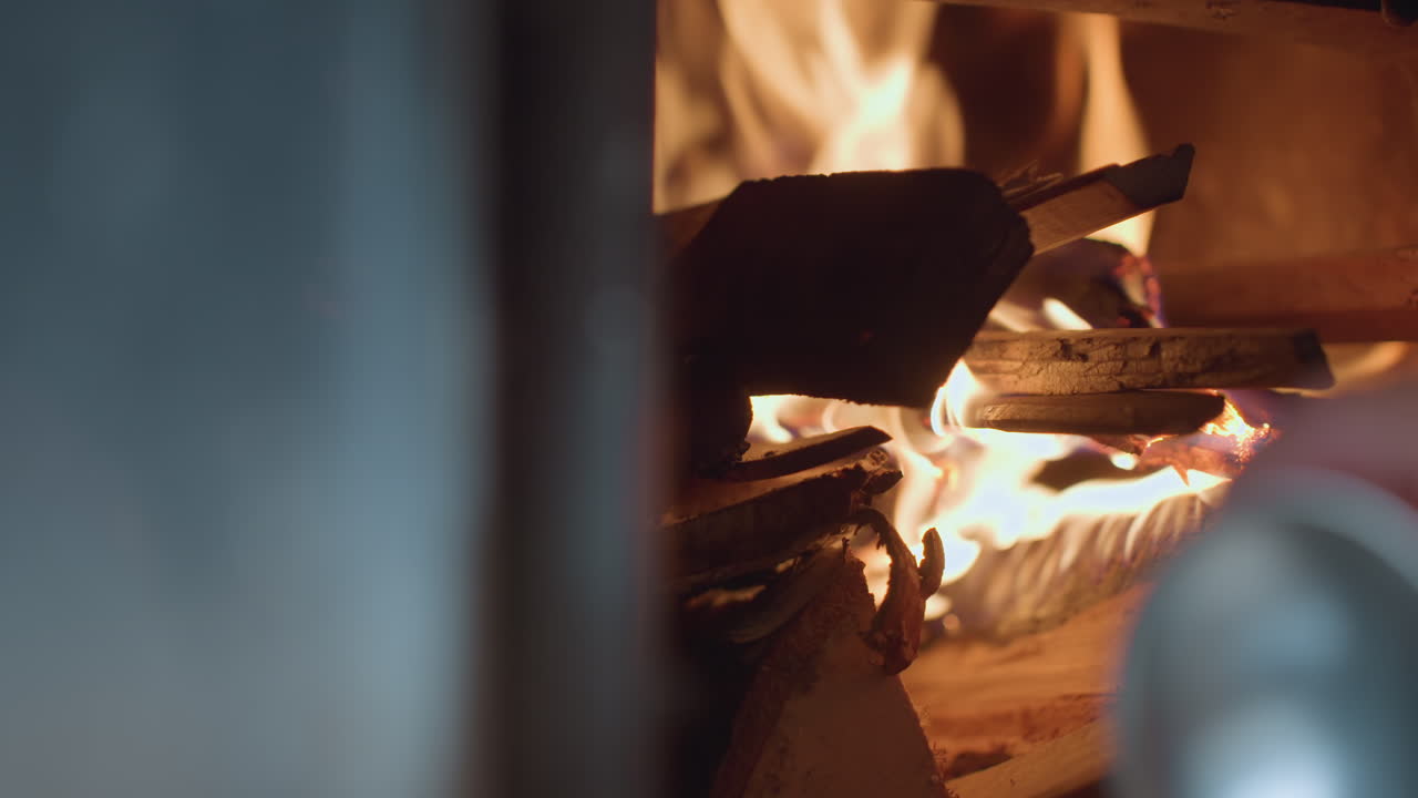 Close up of wood burning in fireplace as flames rise and flicker between stacked logs, fire glows brightly, illuminating wooden textures with soft light and creating warm, rustic indoor atmosphere