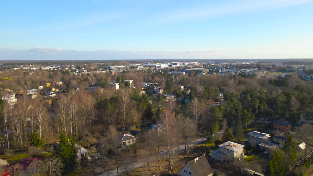 Aerial drone footage flying up and revealing a quiet and nice looking living neighborhood in Laagri Saue district during golden hour spring where leafless trees and pine trees are between small houses
