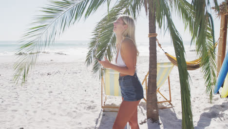mujer caucásica usando su teléfono inteligente en la playa
