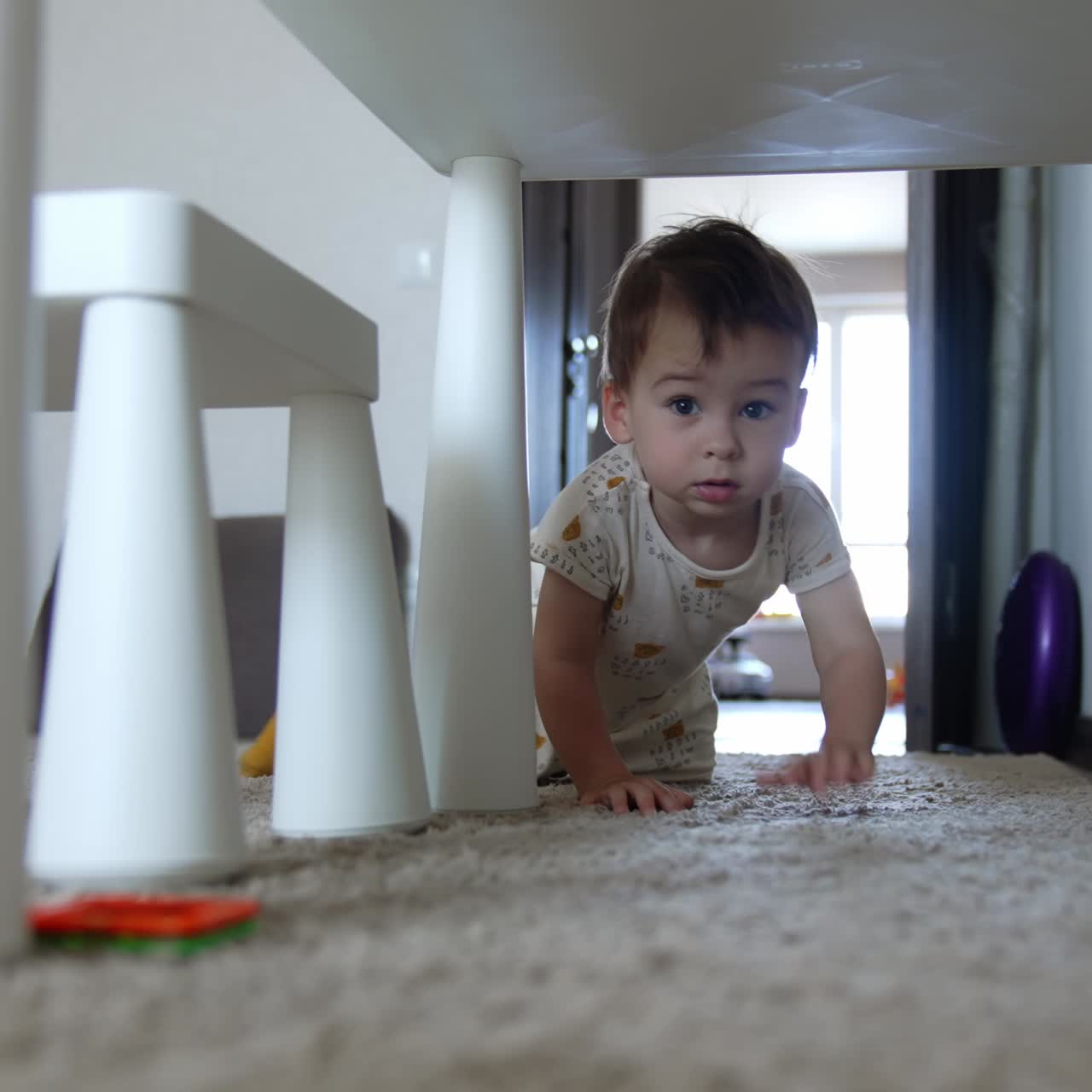 Beautiful lovely baby climbs under the table. Baby boy grabs the toy and moves back