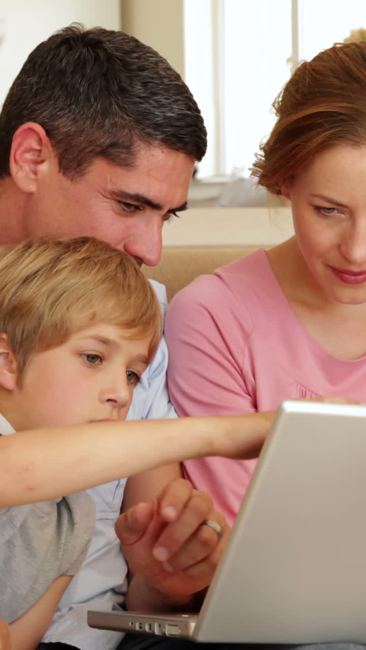 Família feliz sentada no sofá usando o laptop juntos.