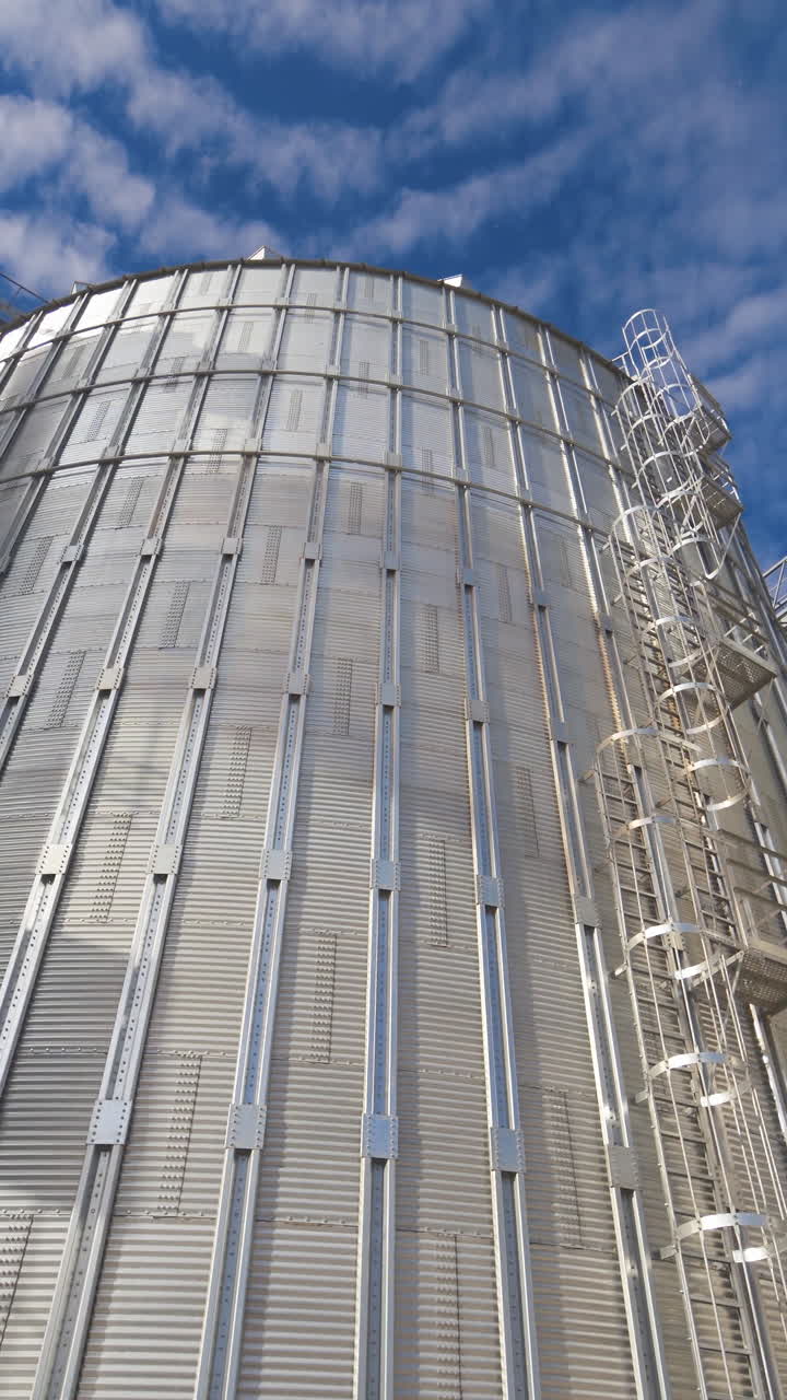Silver storage tanks at sunlight. Large metal grain elevators against blue sky. Modern agro-processing factory. Vertical video