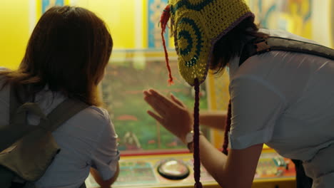 rearview of girl in knitted headwear hitting button at carnival game with friend