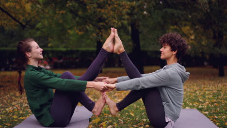 two women practicing partner yoga in a park
