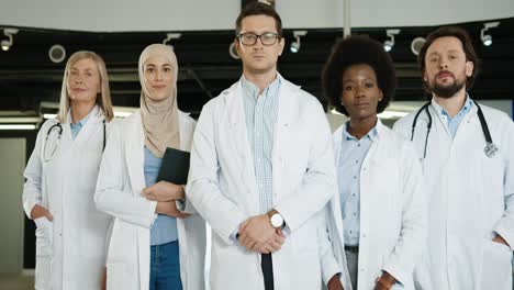 equipo de médicos multiétnicos en abrigos médicos de pie en el laboratorio del hospital y mirando a la cámara