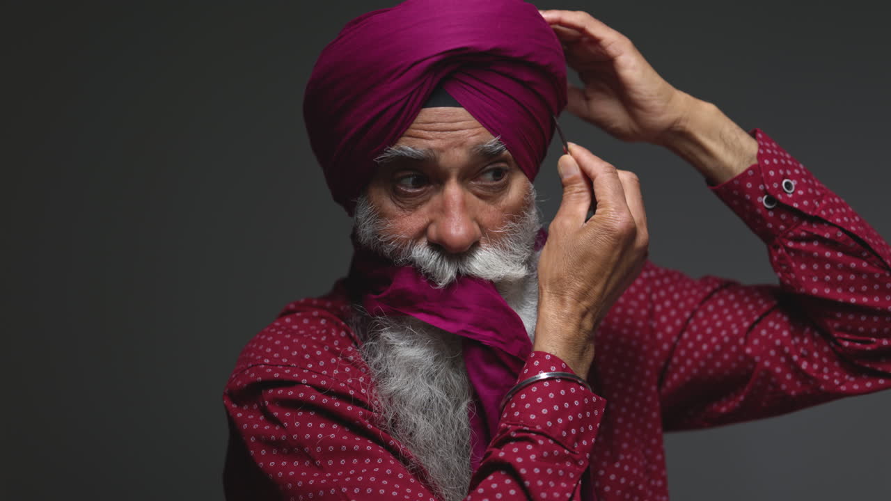 close up bajo clave de estudio de iluminación disparo de un anciano sikh con barba usando aguja salai al ponerse el turbante contra un fondo oscuro disparo en tiempo real