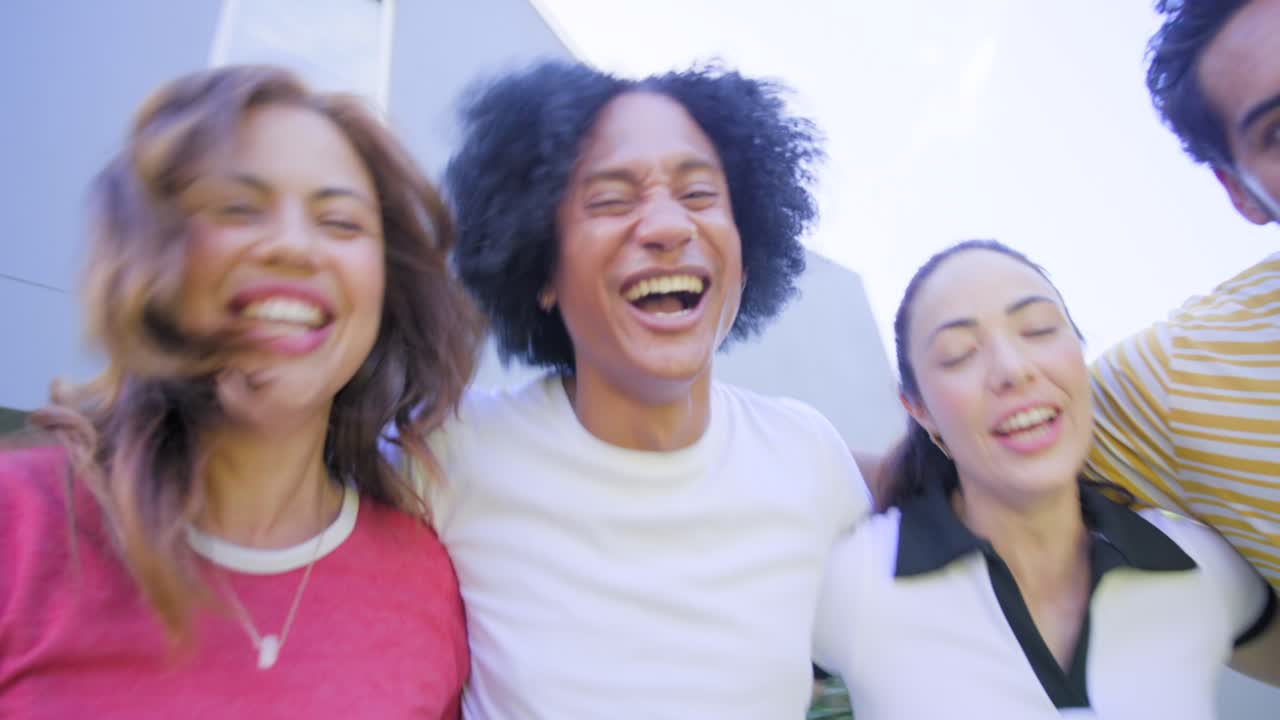Amici di diverse etnie che si avvicinano a una fotocamera a mano bassa, ridono, si chiamano e si divertono all'aperto