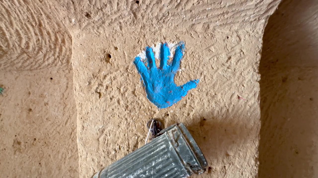 Impressão de mão pintada de azul brilhante representando a Mão de Fátima em um pilar de argila rústico em uma casa-caverna tradicional de Matmata na Tunísia