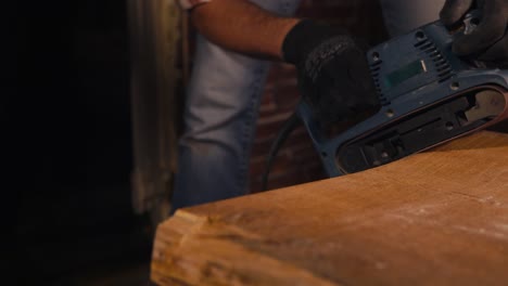 man sanding a wooden table top with a belt sander