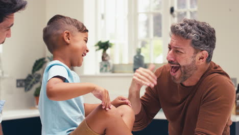 same sex family with two dads in kitchen with son sitting on counter giving parent high five