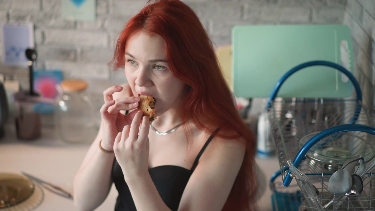 Белая женщина пробует выпечку с любопытным выражением лица у кухонной стойки, крупный план рук и укуса, эклектичная утварь и сушилка для посуды на заднем плане, откровенный момент дегустации с легким удивлением.