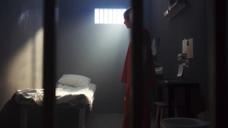 bored prisoner wandering around prison cell, then sitting on bed