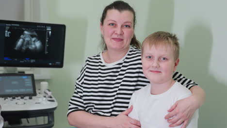 mother and child seated on hospital bed, mother holding child firmly while both smile joyfully, depicting a caring family moment in a medical setting with ultrasound in the background