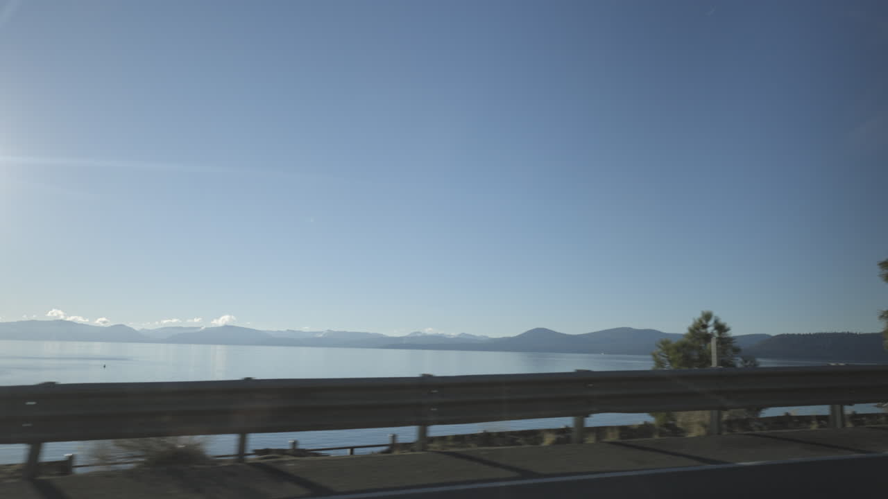 Lake Tahoe passes by beyond the guard rail on the side of the road from the driver side POV