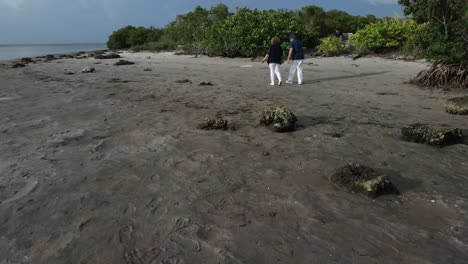 Antena-De-Una-Pareja-Mayor-Divirtiéndose-Caminando-De-Manera-Divertida-En-La-Playa-Durante-Sus-Años-Dorados-Bajo-El-Sol