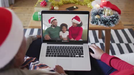 African-american-mother-and-daughter-using-laptop-for-christmas-video-call-with-family-on-screen