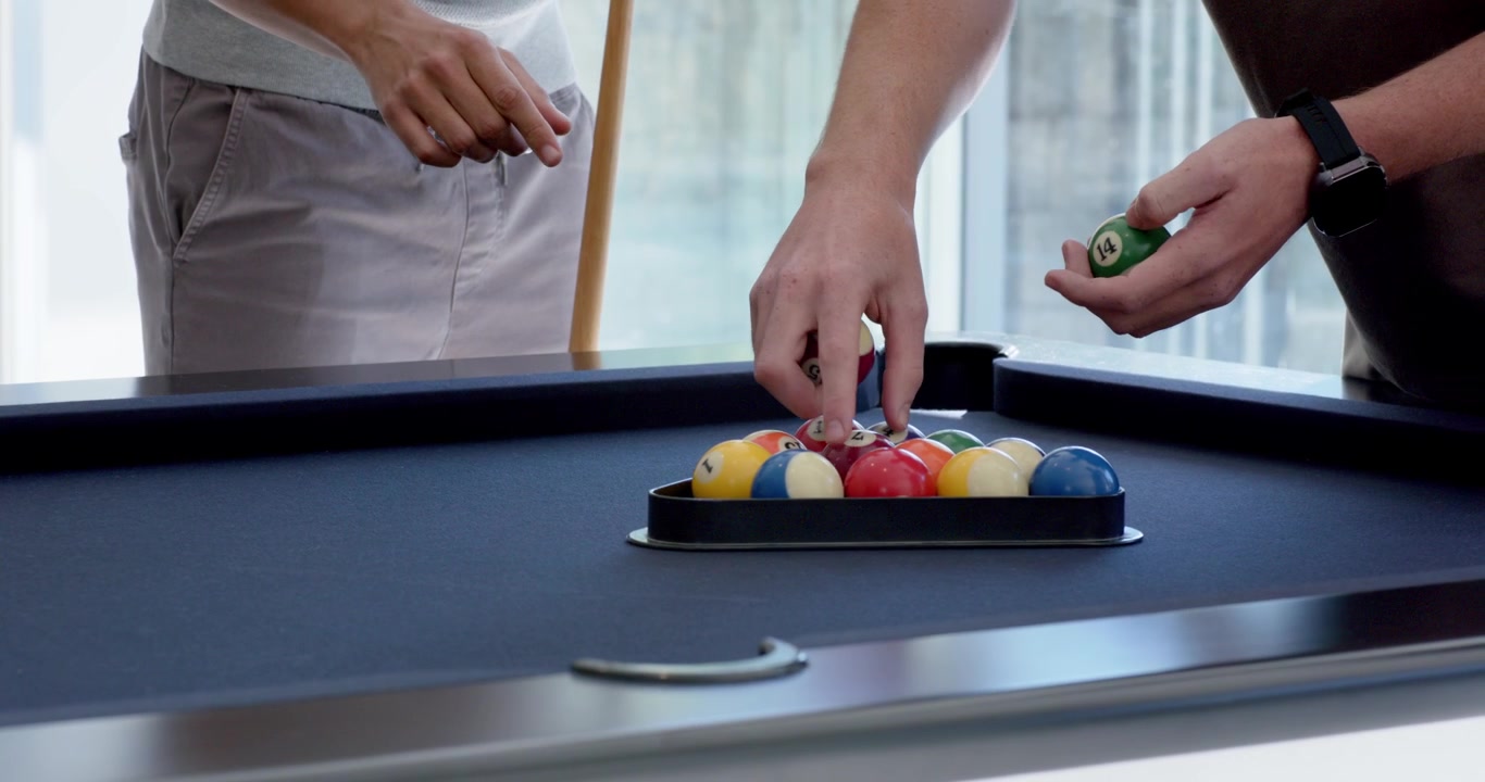 Diverse male friends in home game room racking balls on pool table, preparing first shot