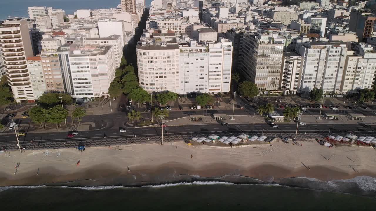 descenso lento aéreo que muestra la playa de copacabana, el bulevar y el barrio visto desde el océano con poco movimiento en las calles por la mañana