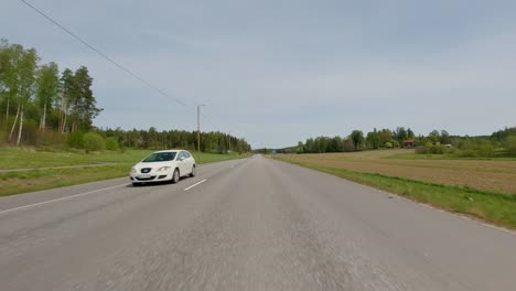 The-road-meanders-through-the-countryside,-with-cars-traversing-along-it,-surrounded-by-lush-green-fields-and-trees-that-dot-the-landscape,-creating-a-picturesque-view