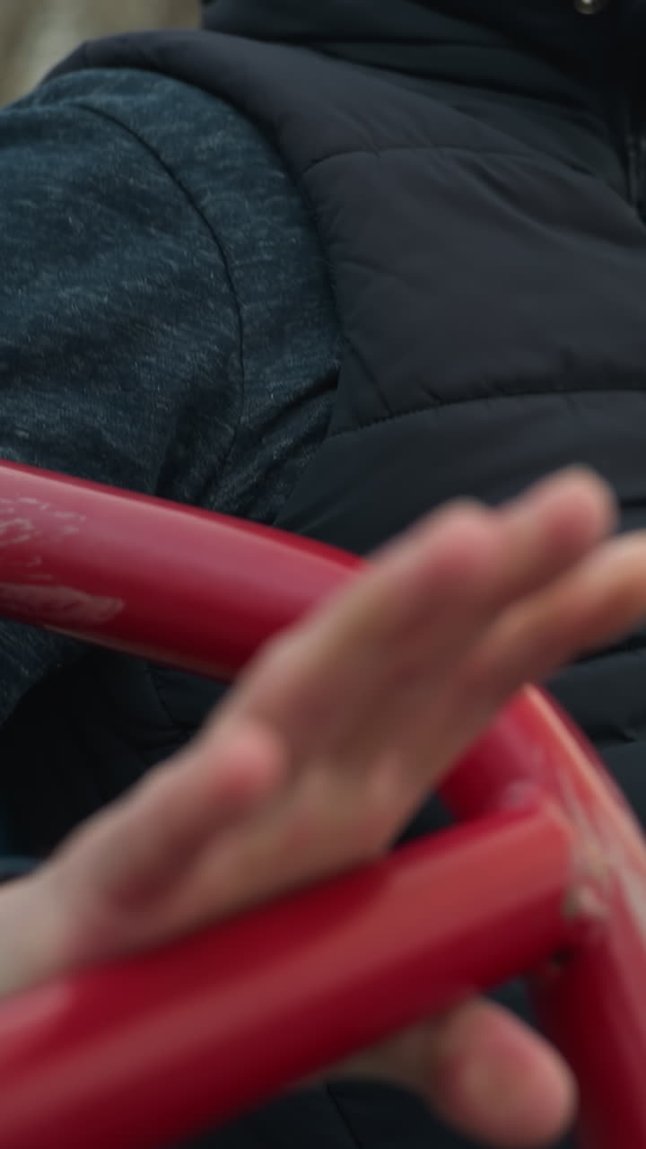 Close up of someone working out on a outdoor equipment, got tired after three pull-ups began to flex his hand on the iron, with blur view of someone in the background
