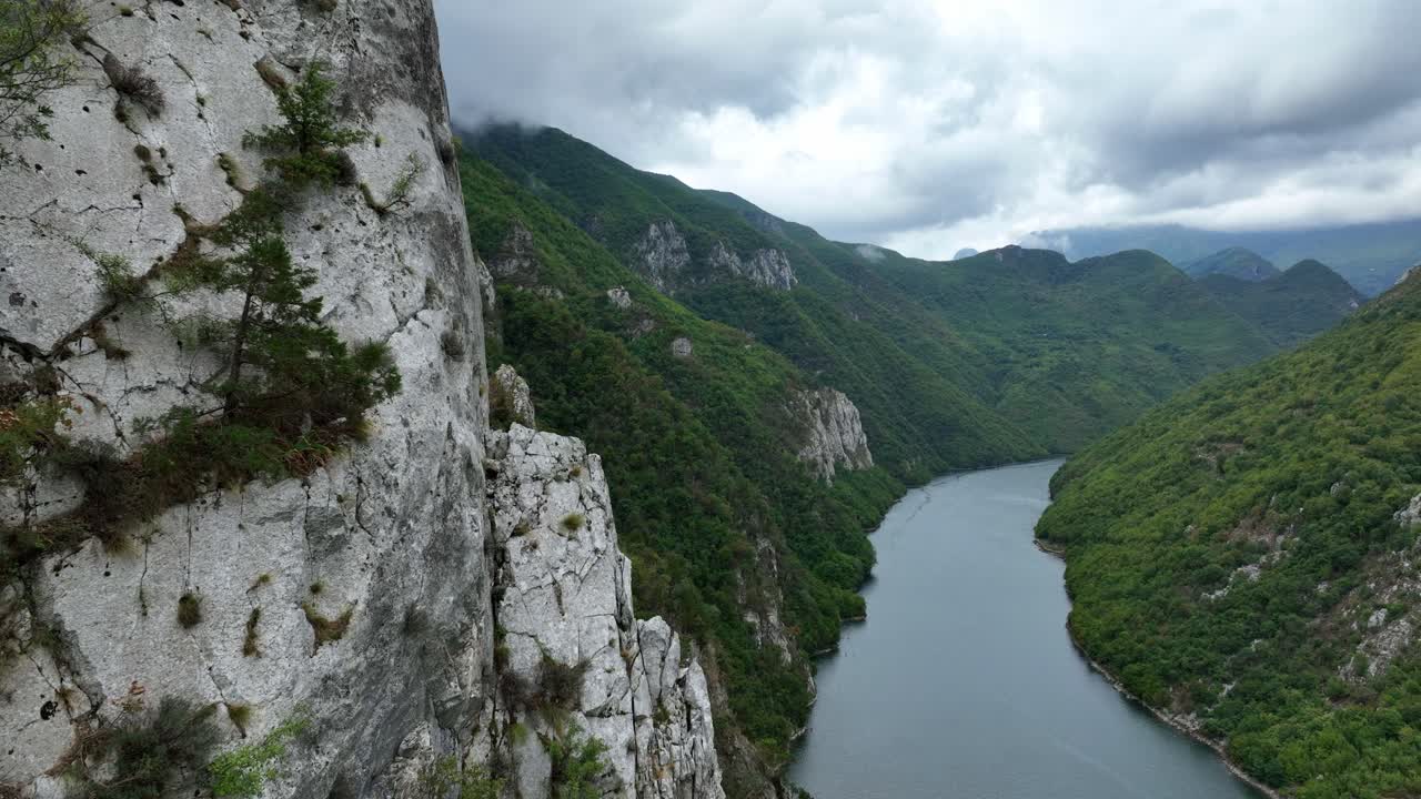 Close proximity flight near white, rocky cliffs overlooking Komani Lake, Albania, a winding lake between lush green mountains