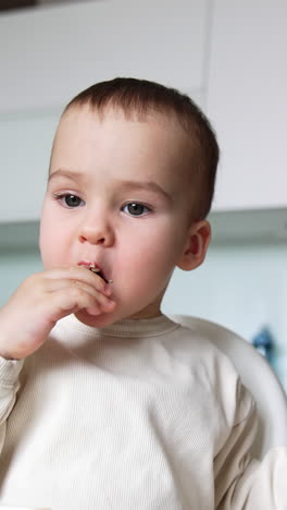 pretty little baby boy slowly chewing the food. smiley kid takes a spoon from mom. low angle view. vertical video
