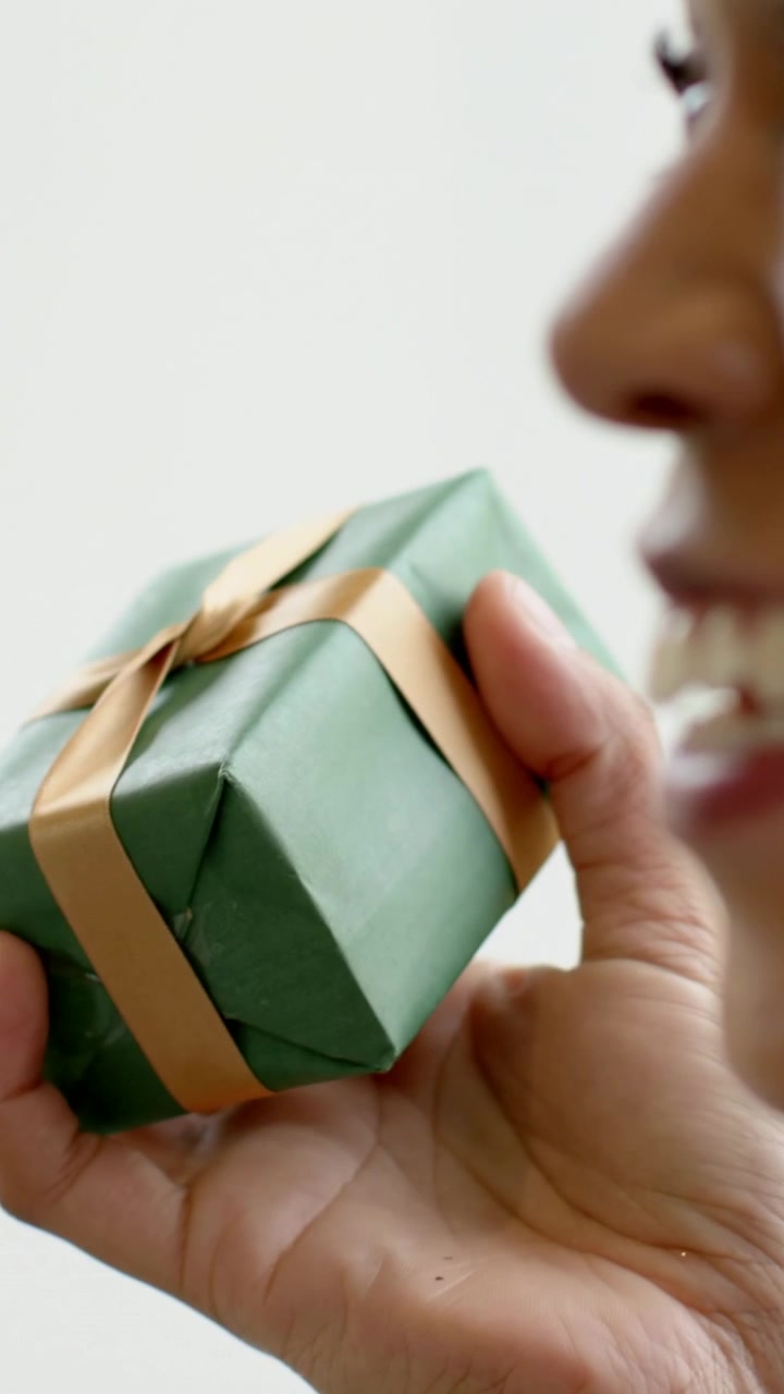 Video verticale: Mano che si allunga per prendere un regalo verde, donna che ispeziona il nastro e sorride, asciugamano.