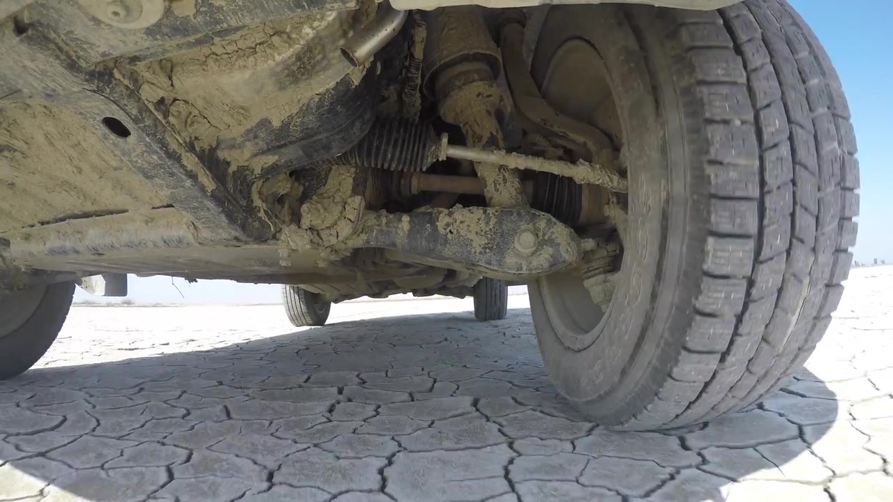 Close-up of Muddy Car Suspension Driving on Dry Cracked Earth