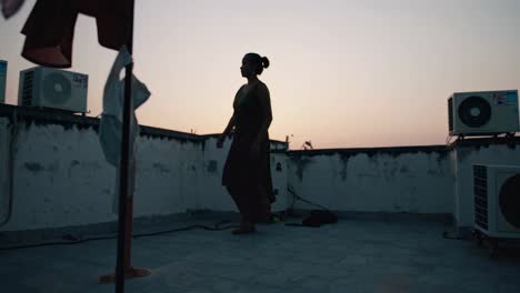 woman walking gracefully on a rooftop at sunset, embodying urban serenity among air conditioning units and hanging laundry, creating a tranquil atmosphere in the cityscape