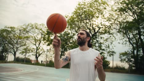 A-middle-aged-man-in-a-white-T-shirt-skillfully-spins-an-orange-basketball-on-his-index-finger-on-a-sports-field-in-summer
