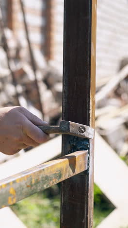 closeup craftsman in camouflage jacket taps on just welded fence parts with hammer in country house yard