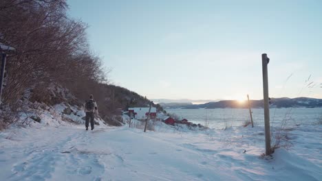 man with backpack walking through snowy path at sunset in vikan, indre fosen, norway