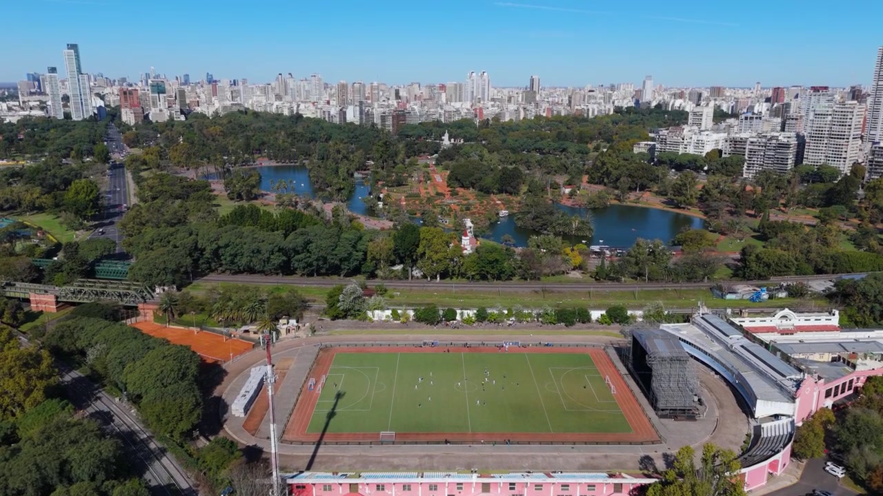 Vista aérea sobre um parque da cidade, campo esportivo e horizonte urbano em um dia claro.