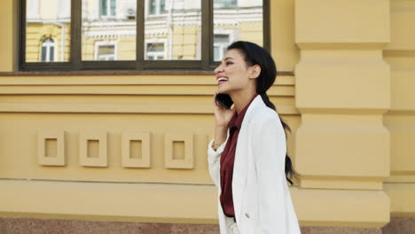 Joyful-mixed-race-businesswoman-walking-with-phone-outdoors.-Lady-laughing