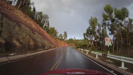 Car-red-sedan,-and-it-is-driving-down-a-wet-road-at-night