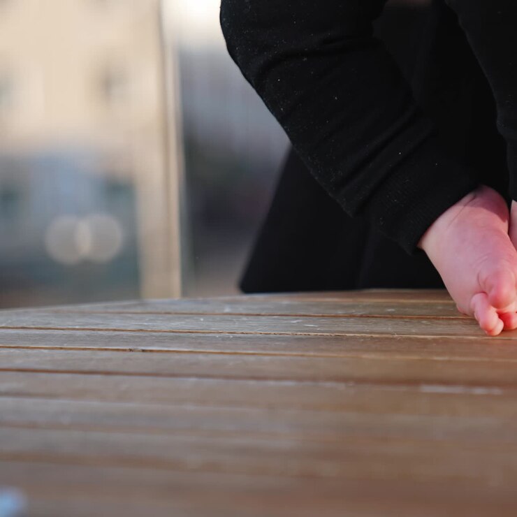 Piedini di un neonato su una superficie di legno. Bambino con pantaloni neri che cammina vicino al tavolo. Sfondo sfocato