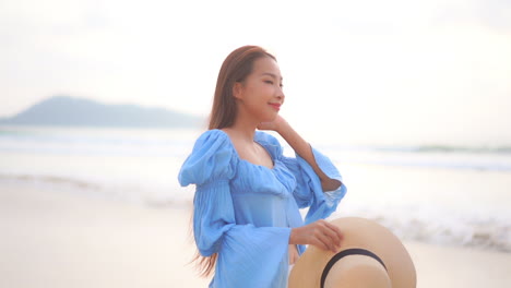 following shot of young asian woman tourist walking along the beachline on sunset, handheld slow-motion, blurred sea tides on background