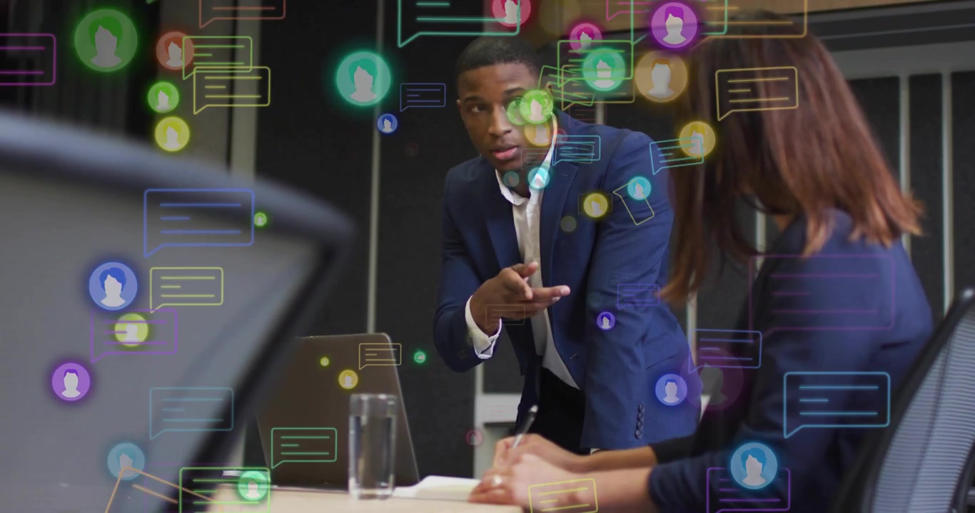 Manager leaning, gesturing in business meeting, causing chat bubbles showing data with woman typing