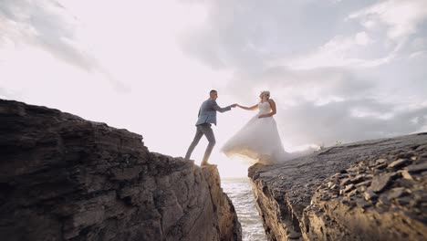 groom goes to bride and gives her a hand. newlyweds on mountainside by the sea