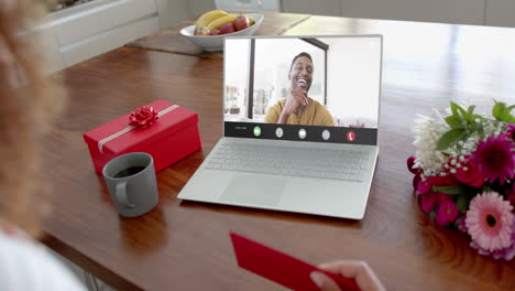 Caucasian-woman-holding-envelope-and-talking-with-biracial-man-on-laptop-screen