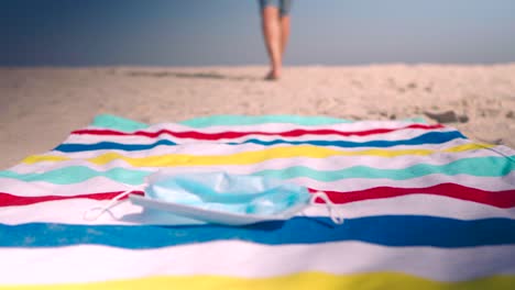 man walks passed beach towel and drops his protective face mask