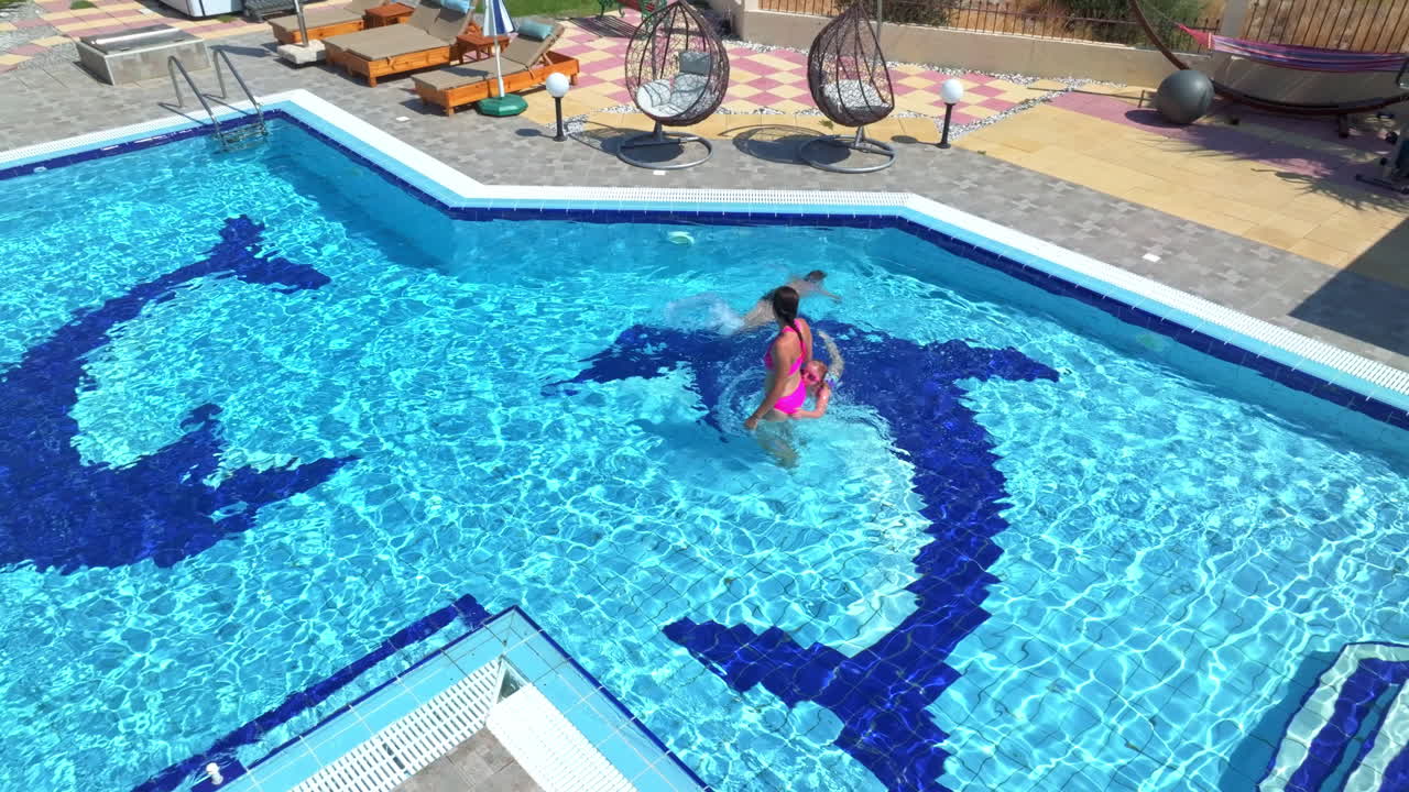 Aerial view orbiting a mom and kids playing in a pool, sunny, summer day
