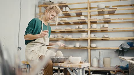 female potter creating at workshop, sculpting crockery on pottery wheel, tracking shot, slow motion