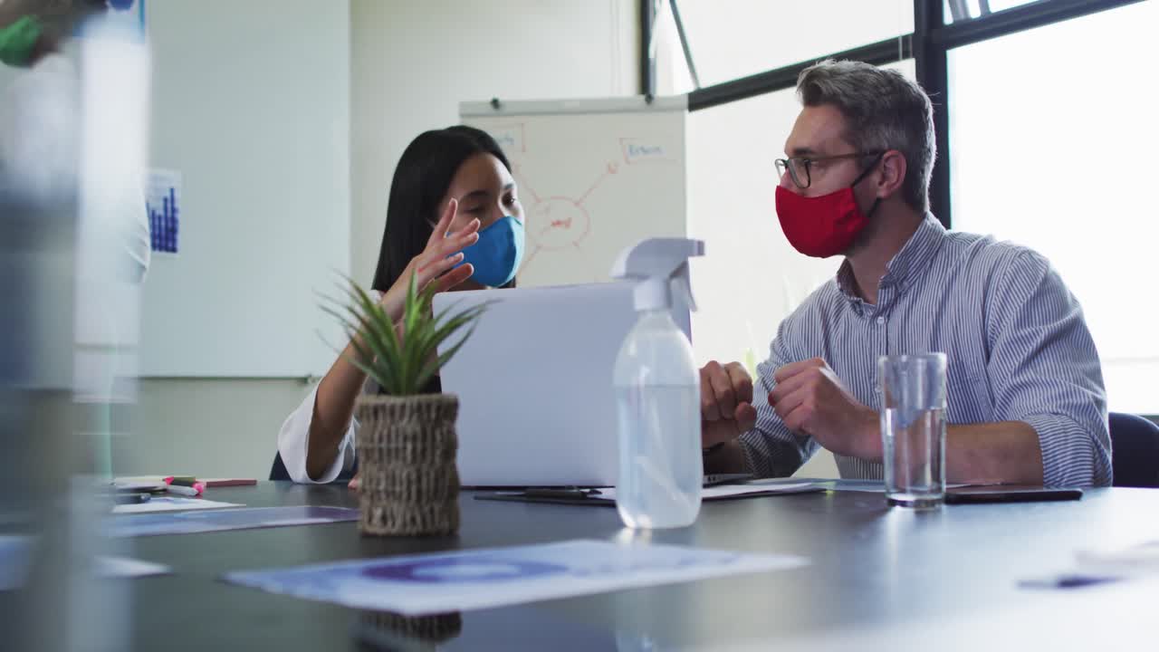 diversos colegas de oficina masculinos y femeninos con máscaras faciales discutiendo sobre una computadora portátil en una oficina moderna