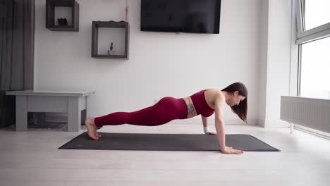 Young-sporty-woman-is-doing-push-ups-exersice-on-mat-in-living-room