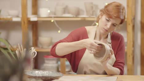 caucasian craftswoman smoothing handmade clay vessel in studio