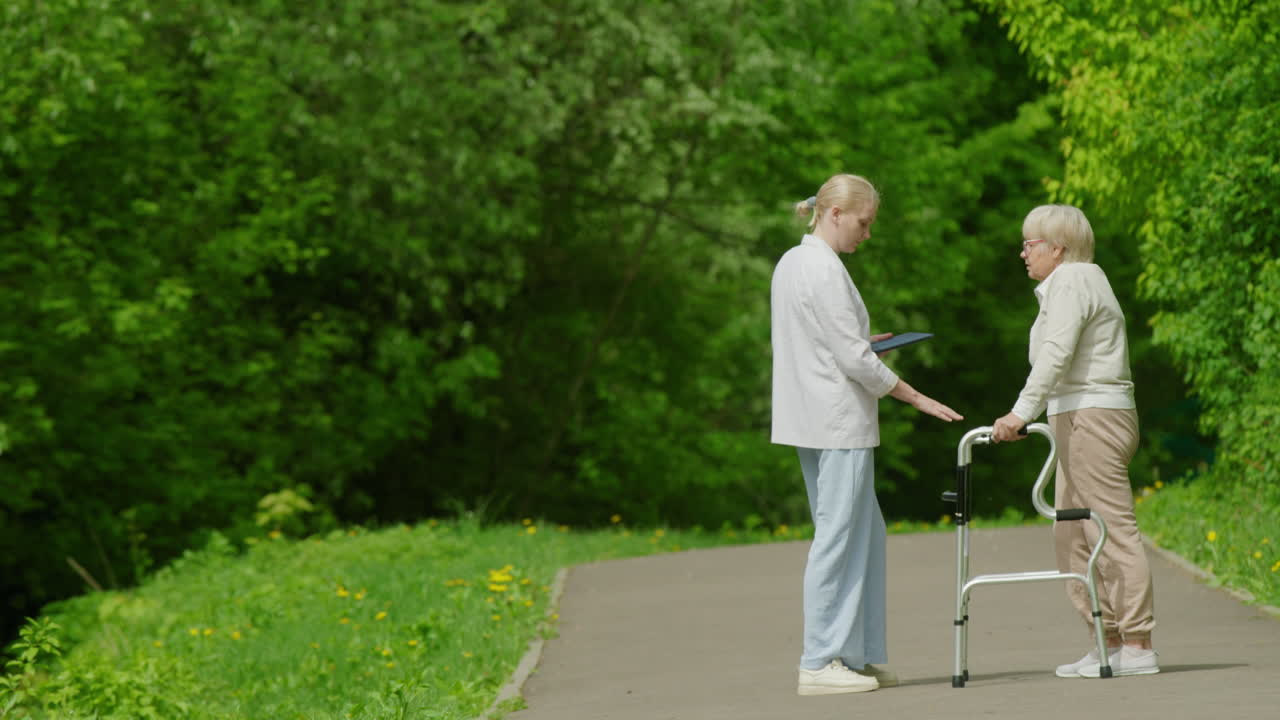 Omsorgsperson hjelper eldre kvinne i en park