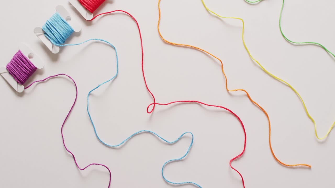 vídeo de seis bobinas de hilos de bordado de colores desenrollados sobre un fondo blanco
