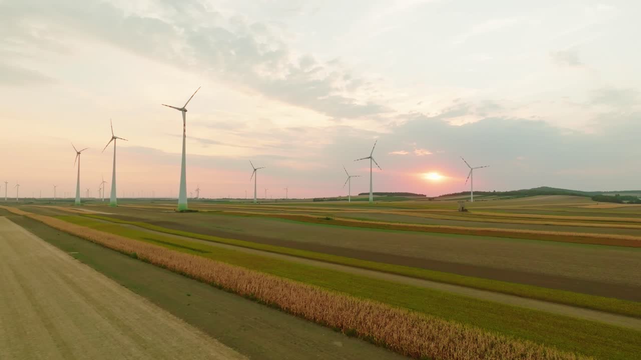 어두워지면서 넓은 농경지 위에 서 있는 풍력 터빈의 공중 풍경, 해가 지는 하늘을 배경으로 자연과 재생 가능한 에너지의 조화로운 혼합을 포착합니다.